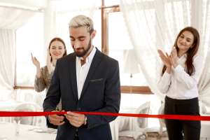 two women are clapping hands when handsome business man is officially cutting red ribbon